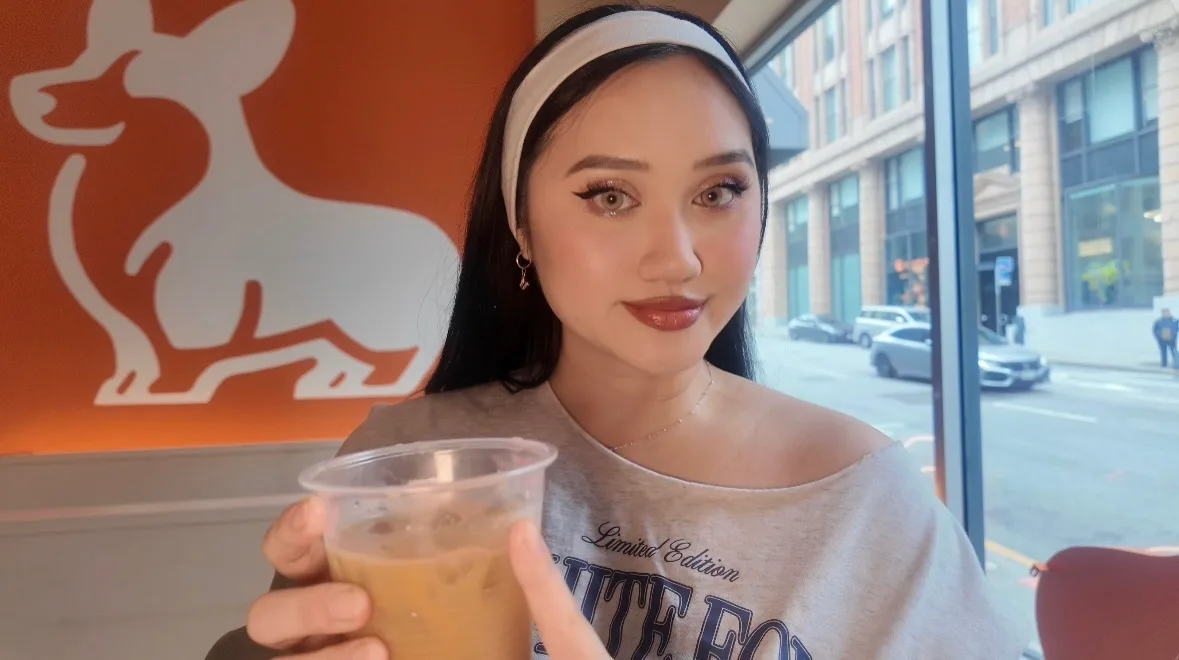 Angela holding an iced drink in front of the Corgi Cafe mural